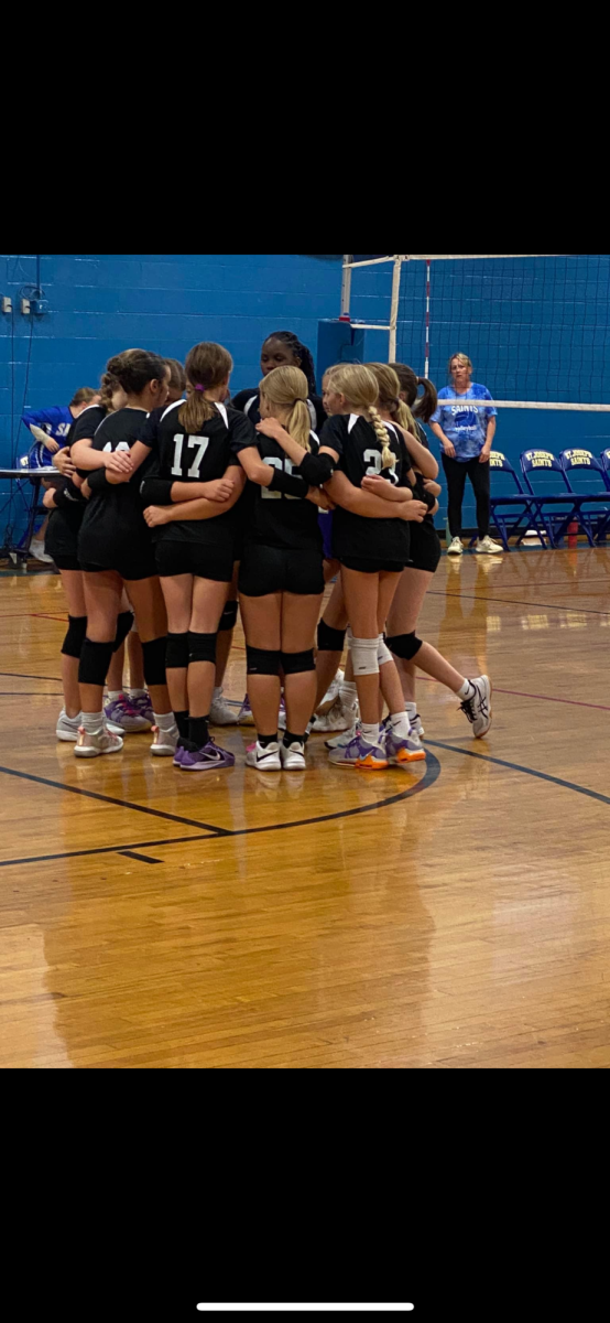 BGJHS volleyball players celebrate after scoring a game point against the Saints, and discussing any new plays or strategies useful win the game. 