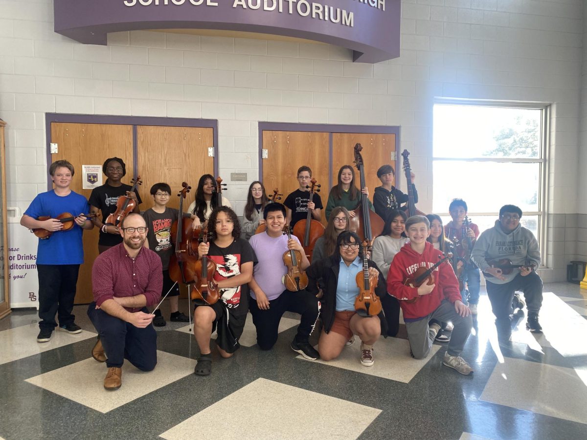 7th grade strings students, standing in the lobby holding their instruments, at BGJH